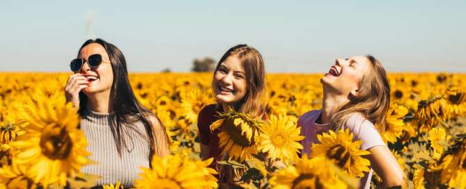 3x girls in a sunflower field laughing and looking into the blue sky