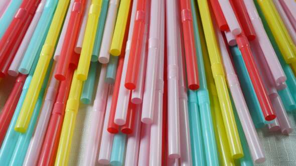 Colourful straws including yellow, red, pink and aqua lay together facing downward