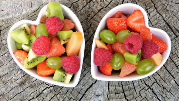 Fresh fruit containing grapes, raspberries, strawberries and kiwi fruit in 2 heart shaped bowls