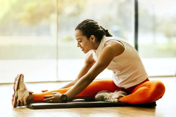 Woman sitting while stretching and doing yoga wearing orange tights and white singlet