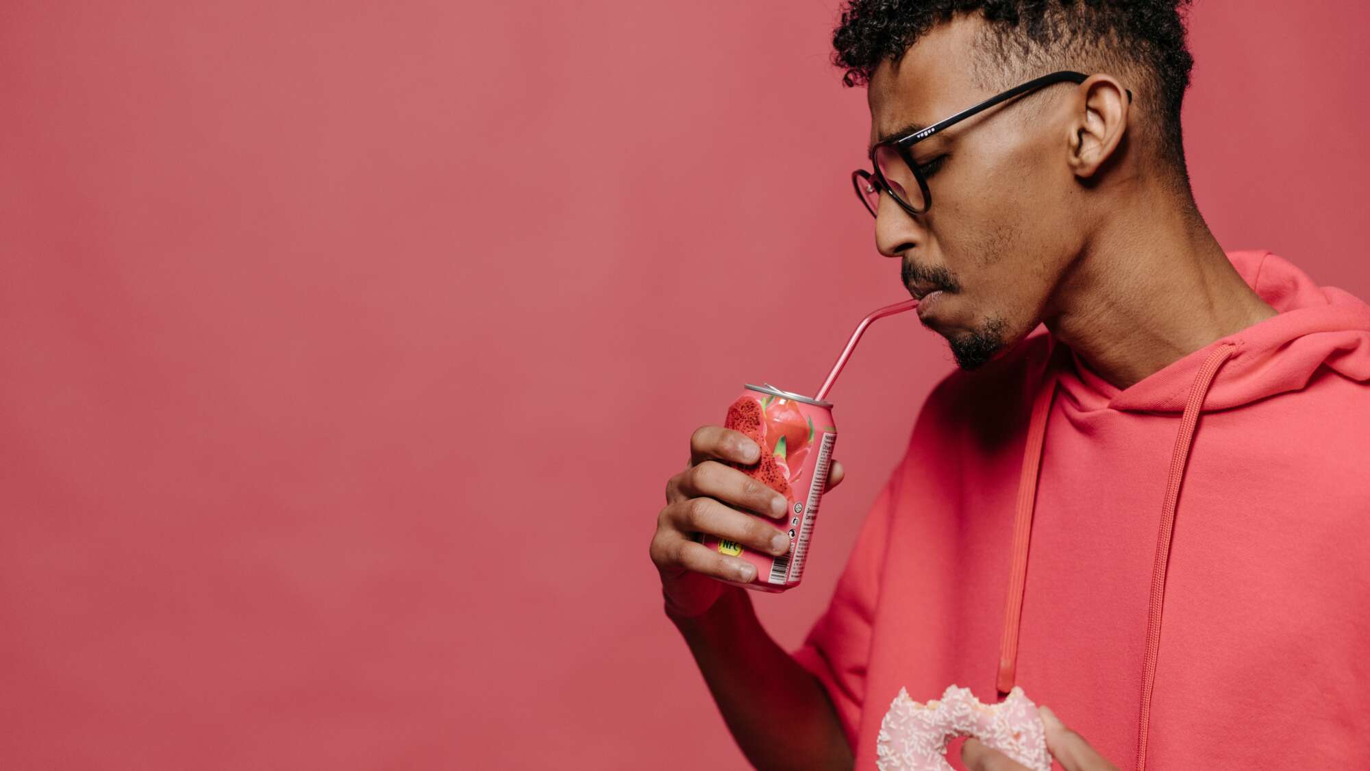 pink background with young adult drinking from a aluminum can of soft drink with a pink drinking plastic draw looking at the can