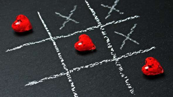 Blackboard, playing naughts and crosses, but with hearts instead of naughts. Diagonal 3x in a row hearts.