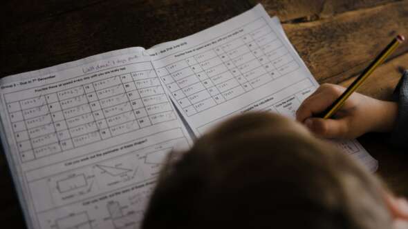Child completing pages of math homework on a timber table