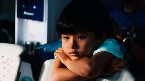 Young boy resting on the back of chair looking disappointed/sad