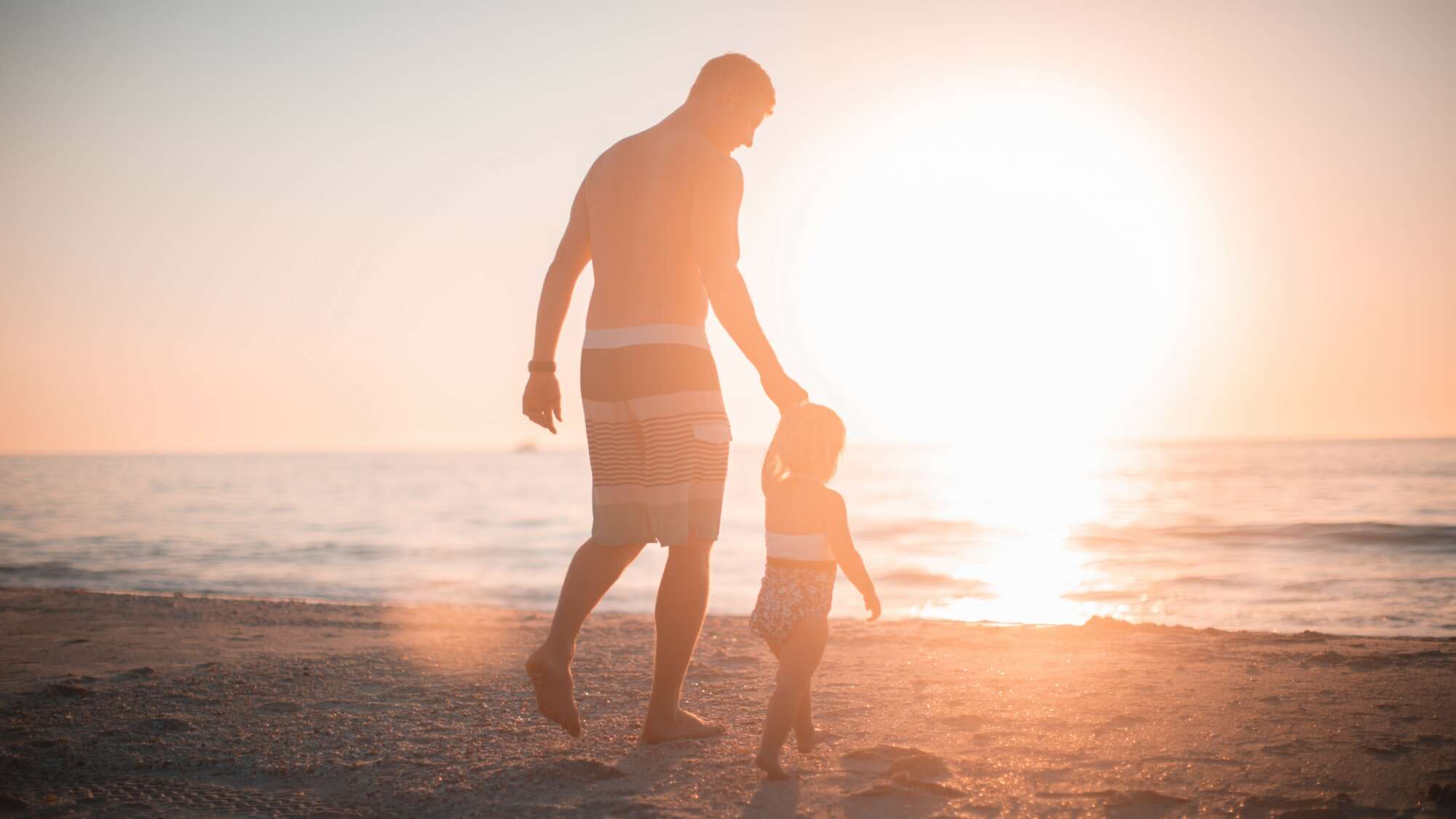 Father and daughter holding hands walking on the beach toward the water