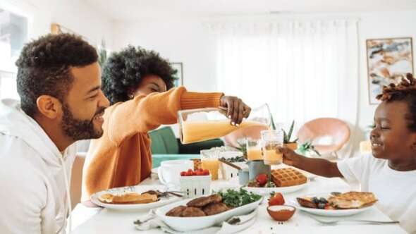 Family eating breakfast together and pouring juice into glass