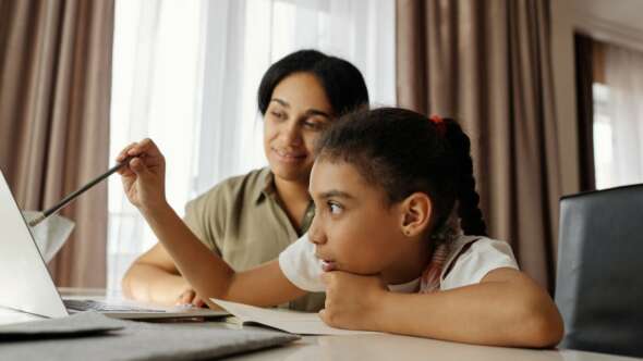 Mother assisting daughter with homework at the dining room table with brown curtains in the background