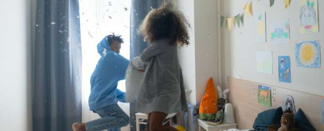 Brother and sister pillow fight with feathers in the childhood room
