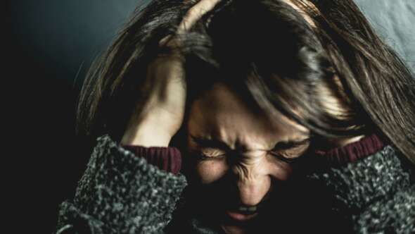 Woman with black hair wearing grey sweater holding her hair forcefully and stressed expression on her face