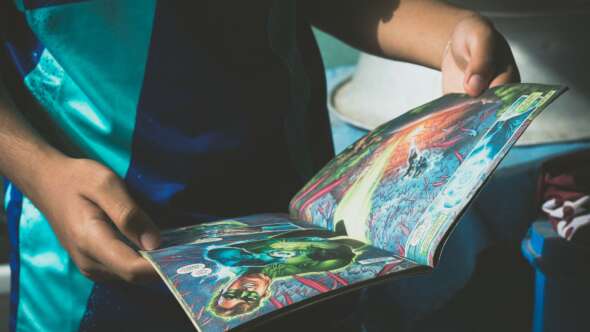 Child in teal and blue school uniform close up shot of reading comic book featuring Green Lantern