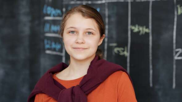 Girl in front of a blackboard smiling and wearing an orange tshirt