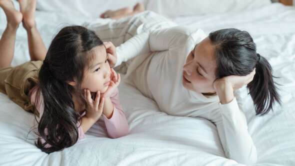 Mother and daughter on bed while mother combs back share of girl