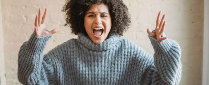 Woman with brown curly hair with hands in the air and her mouth open wide screaming