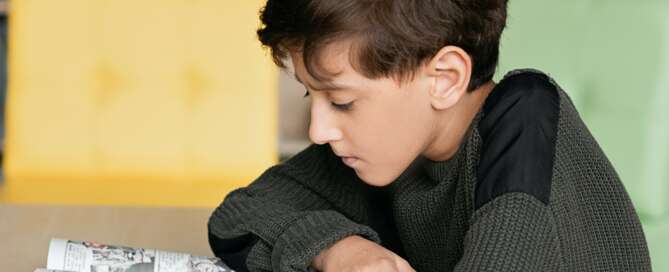 Young child wearing a dark sweater reading comic book