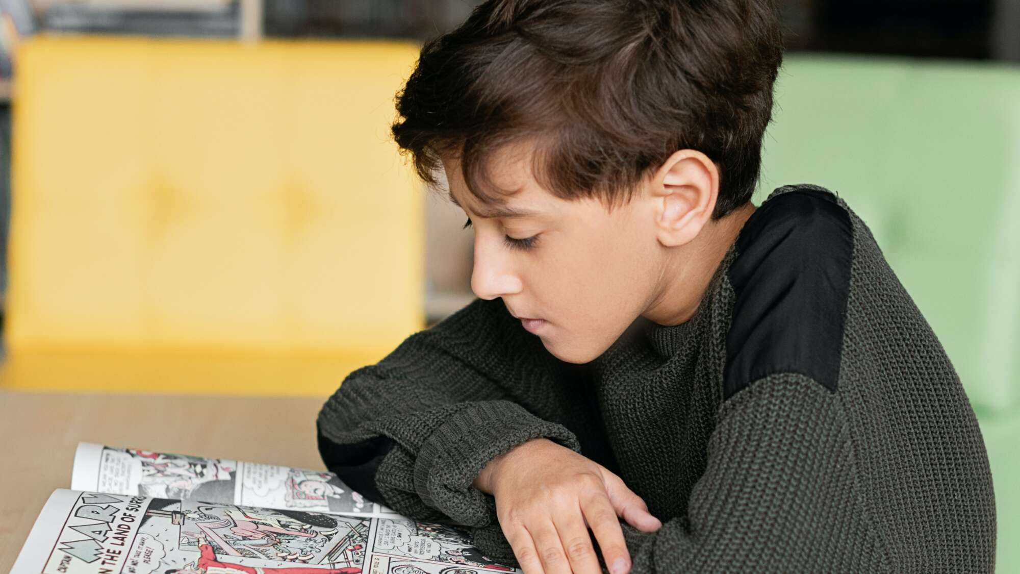 Young child wearing a dark sweater reading comic book