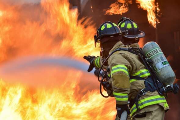 Two firefighters with a water hose attempting to extinguish large fire.