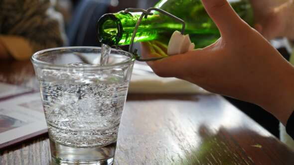 pouring a glass of water with a green glass bottle