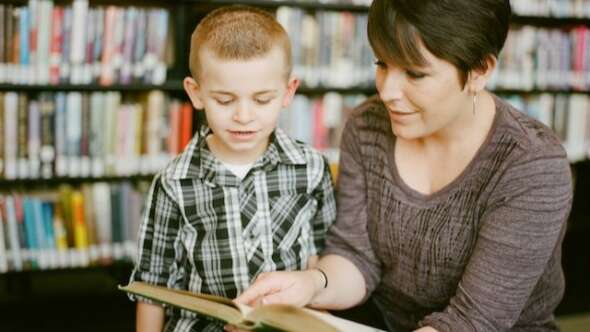 Teacher with short dark hair looking into a book with a student