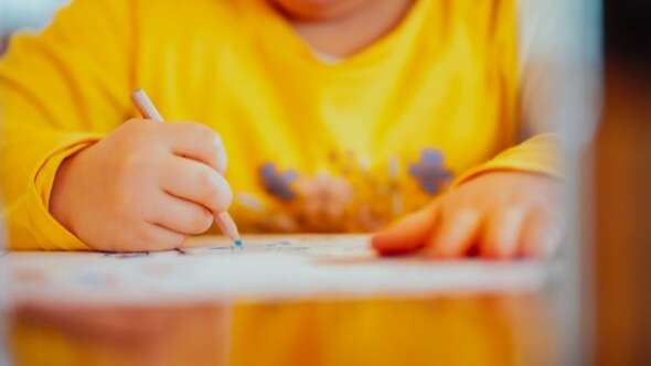 Child in yellow shirt drawing on paper