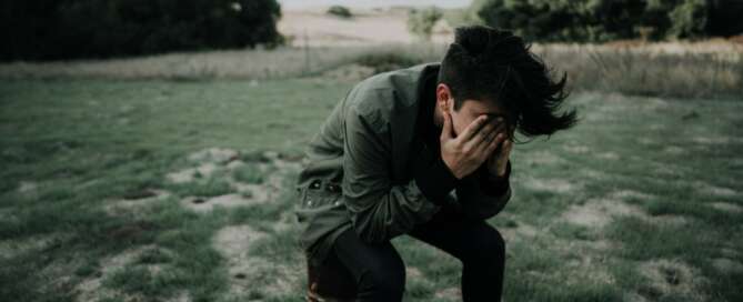 Young boy sitting in a field with his hands over his eyes