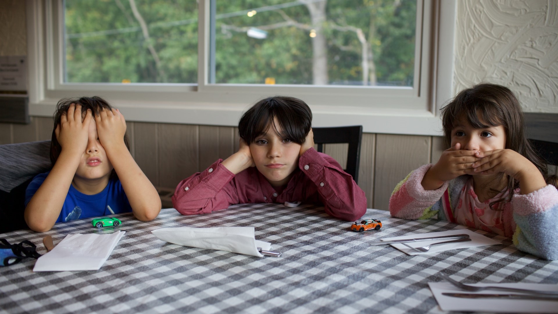 Three children covering their eyes, ears and mouth at a dining table