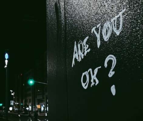 Graffiti on the side of a dark wall in the city stating: Are you okay?