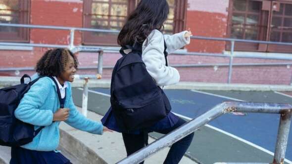Two girls running to school through the courtyard in school uniform